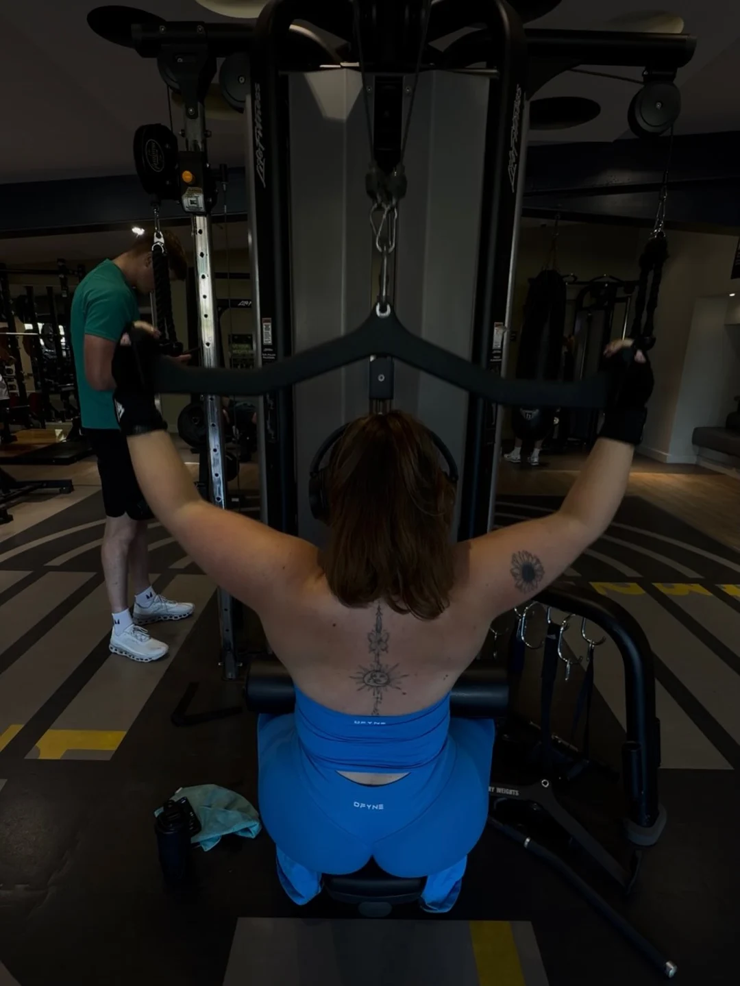 Em in blue gymwear using a back training machine